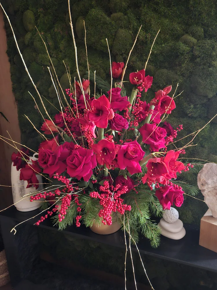 Winter statement arrangement of red amaryllis, roses, berries and gold twigs against a moss wall